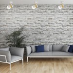 Lampa sufitowa Anillo w kolorze białym z jednym reflektorem GU10. Ujęcie z góry, pokazujące lampę zamontowaną na suficie w nowoczesnym wnętrzu z szarymi meblami i kamienną ścianą. Lampa ma prosty, minimalistyczny design.