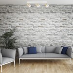 Lampa sufitowa Anillo w kolorze białym z trzema ruchomymi reflektorami GU10. Zamontowana na prostokątnej podstawie, prezentuje minimalistyczny design. W tle widoczna szara sofa z niebieskimi poduszkami oraz kamienna ściana.