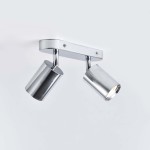 Lampa sufitowa Belize z dwoma reflektorami w chromowanym wykończeniu. Ujęcie z boku, z zamocowaną na ścianie podstawą. Reflektory cylindryczne, skierowane w różne strony, podkreślają nowoczesny design. Tło jasne, jednolite.