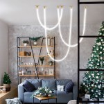 Lampa wisząca Rope Light 1xLED/50W w kolorze złotym, z dwoma smukłymi, białymi przewodami świetlnymi, zawieszona w nowoczesnym wnętrzu z szaro-beżowymi ścianami, w pobliżu dekoracji świątecznych i sofy.