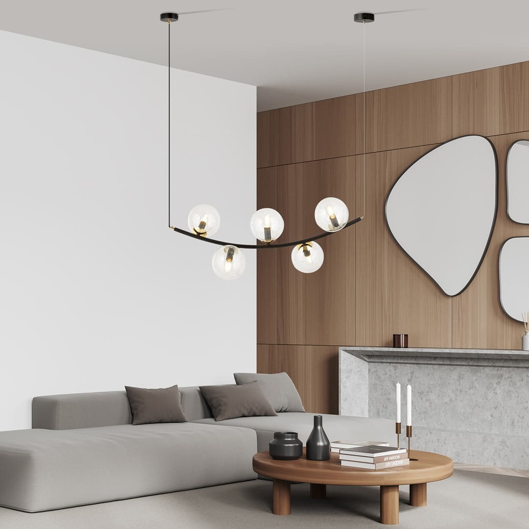 Lampa wisząca Ritz z pięcioma kulistymi kloszami w kolorze czarnym i transparentnym, zawieszona na cienkim przewodzie. W tle nowoczesny salon z drewnianą ścianą i okrągłym stolikiem.