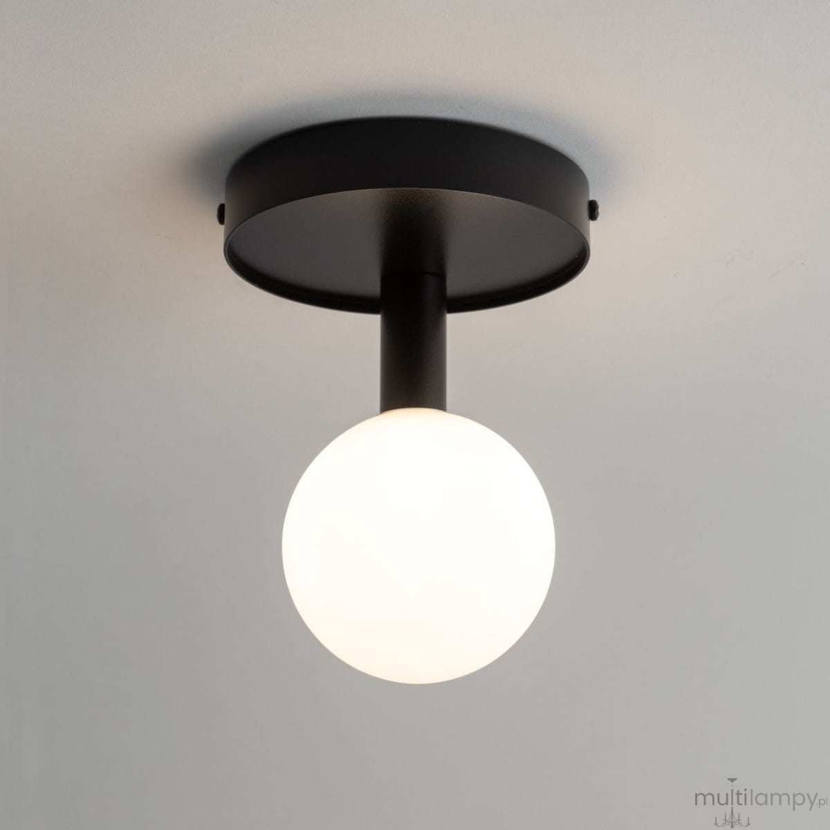Lampa sufitowa Perla w kolorze czarnym i białym, z okrągłym kloszem z mlecznego szkła. Ujęcie od dołu, z widocznym mocowaniem sufitowym. Prosta, nowoczesna konstrukcja, idealna do różnych wnętrz.