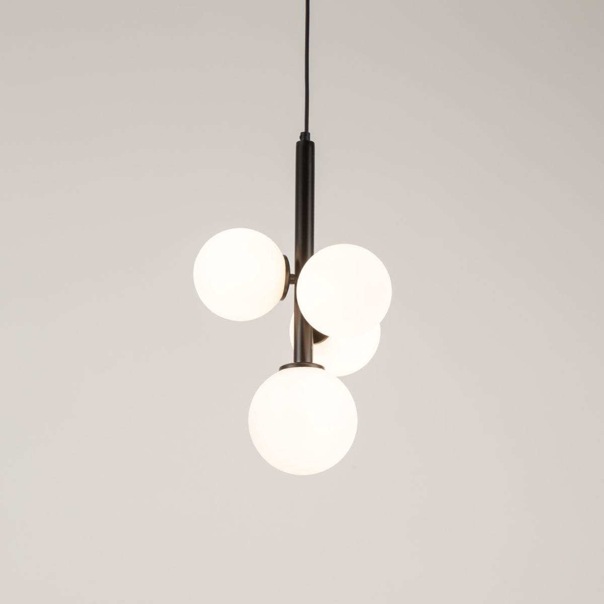 Lampa wisząca Perla z czarnym metalowym uchwytem i czterema białymi, półprzezroczystymi kulami. Produkt zawieszony, z widocznym kablem. Prosty, nowoczesny design, idealny do wnętrz.