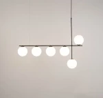 Lampa wisząca Silia z sześcioma okrągłymi kloszami w białym kolorze, umieszczona na czarnym, poziomym stelażu. Ujęcie frontalne, lampa zawieszona na cienkim przewodzie, z jedną kulą umiejscowioną wyżej. Tło jasne, jednolite.