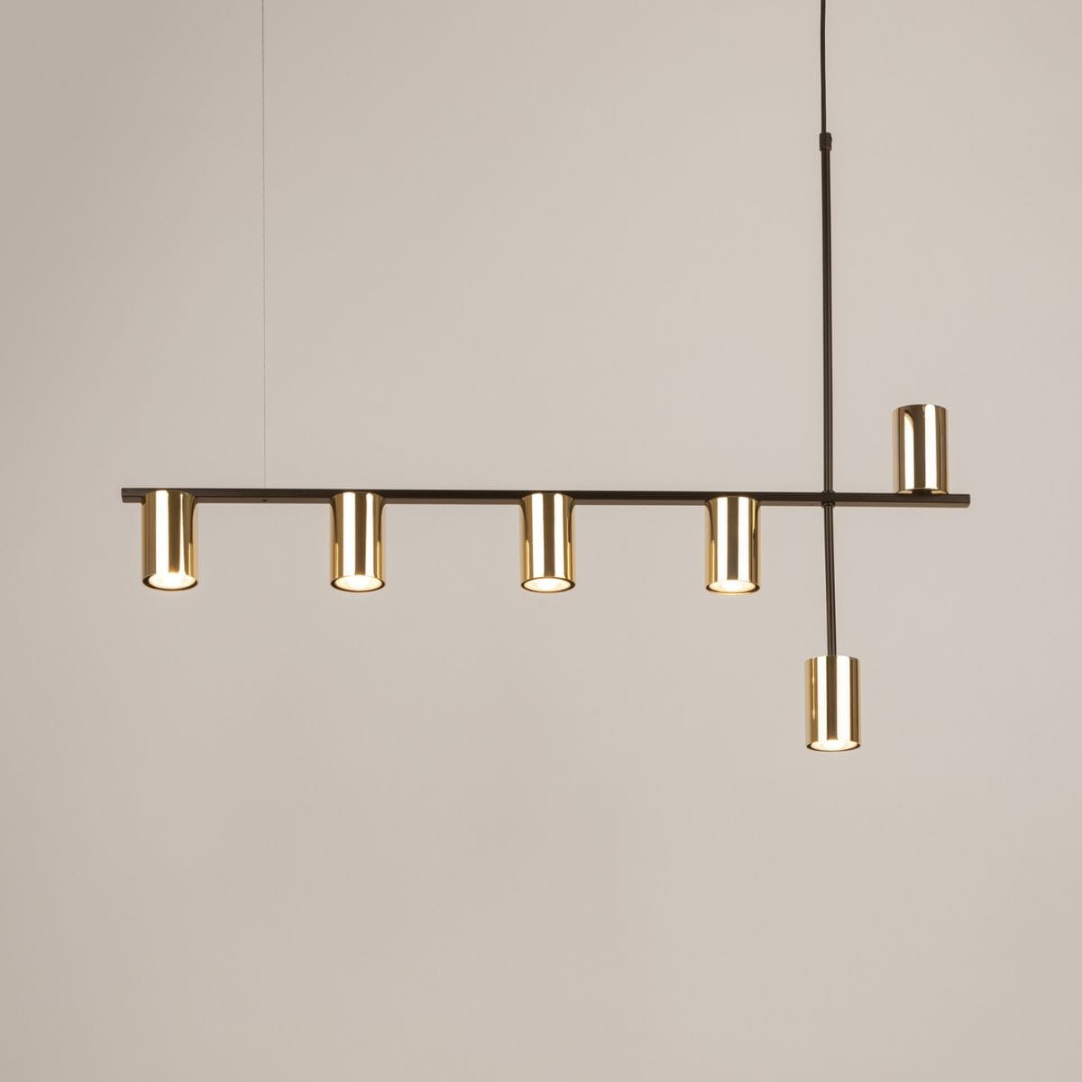 Lampa wisząca Vendo z mosiężnymi kloszami, montowana na czarnym stelażu. Posiada sześć uchwytów na żarówki GU10, zawieszona poziomo. Klosze mają cylindryczny kształt, co nadaje nowoczesny wygląd. Tło jasne, neutralne.