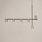Lampa wisząca Vendo z mosiężnymi kloszami, montowana na czarnym stelażu. Posiada sześć uchwytów na żarówki GU10, zawieszona poziomo. Klosze mają cylindryczny kształt, co nadaje nowoczesny wygląd. Tło jasne, neutralne.