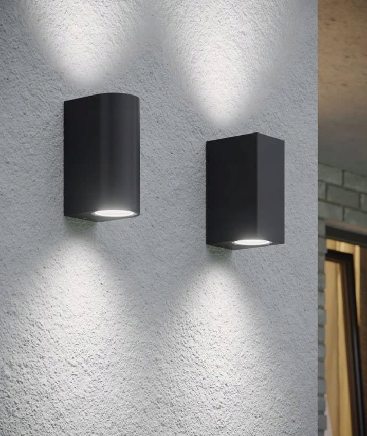 Kinkiet elewacyjny Luna Duo w kolorze grafitowym, składający się z dwóch lamp w różnych kształtach (okrągłej i prostokątnej). Zainstalowany na jasnej ścianie, emitujący światło w górę i w dół. Idealny do oświetlenia ogrodu i elewacji budynku.
