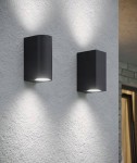 Kinkiet elewacyjny Luna Duo w kolorze grafitowym, składający się z dwóch lamp w różnych kształtach (okrągłej i prostokątnej). Zainstalowany na jasnej ścianie, emitujący światło w górę i w dół. Idealny do oświetlenia ogrodu i elewacji budynku.