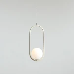 Kremowa lampa wisząca Riva o jednopunktowym źródle światła, z okrągłym kloszem w białym kolorze, umieszczona w metalowej ramie w kształcie elipsy. Produkt zawieszony na cienkim przewodzie, na jednolitym tle.