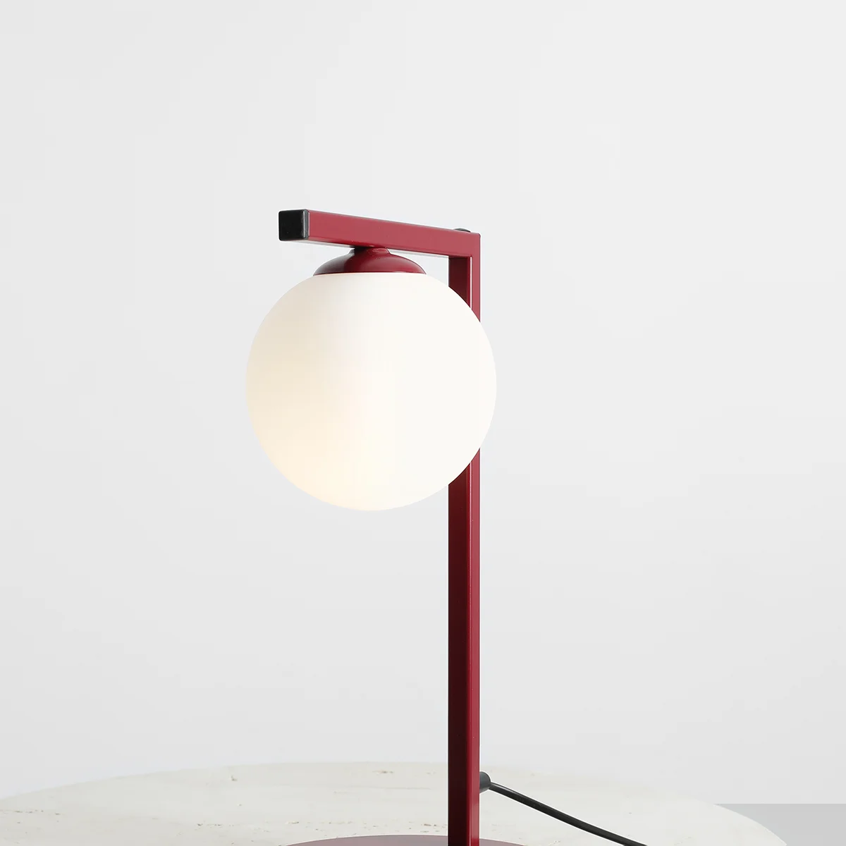 Lampa stołowa Zac 1-punktowa w kolorze czerwonym. Konstrukcja z metalowym stelażem i okrągłą kloszem z białego szkła. Ujęcie frontalne, lampa stoi na płaskiej powierzchni, z widocznym kablem zasilającym.