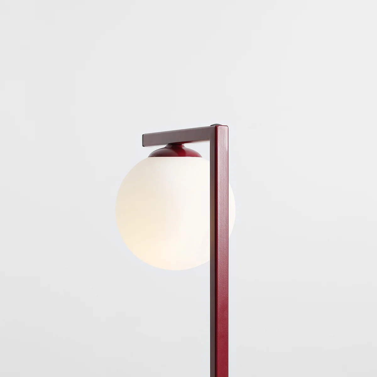 Czerwona lampa stołowa Zac 1-punktowa z białym, okrągłym kloszem. Ujęcie z boku, pokazujące prostą, metalową konstrukcję z poziomą poprzeczką. Klosz umieszczony na górze, lekko przemawia przez matowe szkło. Tło jednolite, jasne.