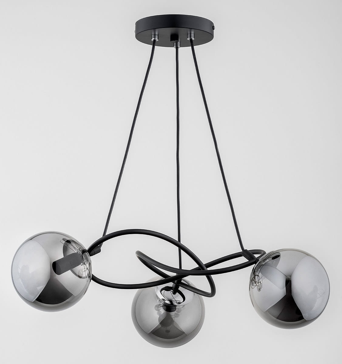 Lampa wisząca Velta z trzema kulistymi kloszami w kolorze chromu, zawieszona na czarnych przewodach. Klosze mają gładką, błyszczącą powierzchnię. Produkt zamontowany na okrągłej podstawie sufitowej w kolorze czarnym.