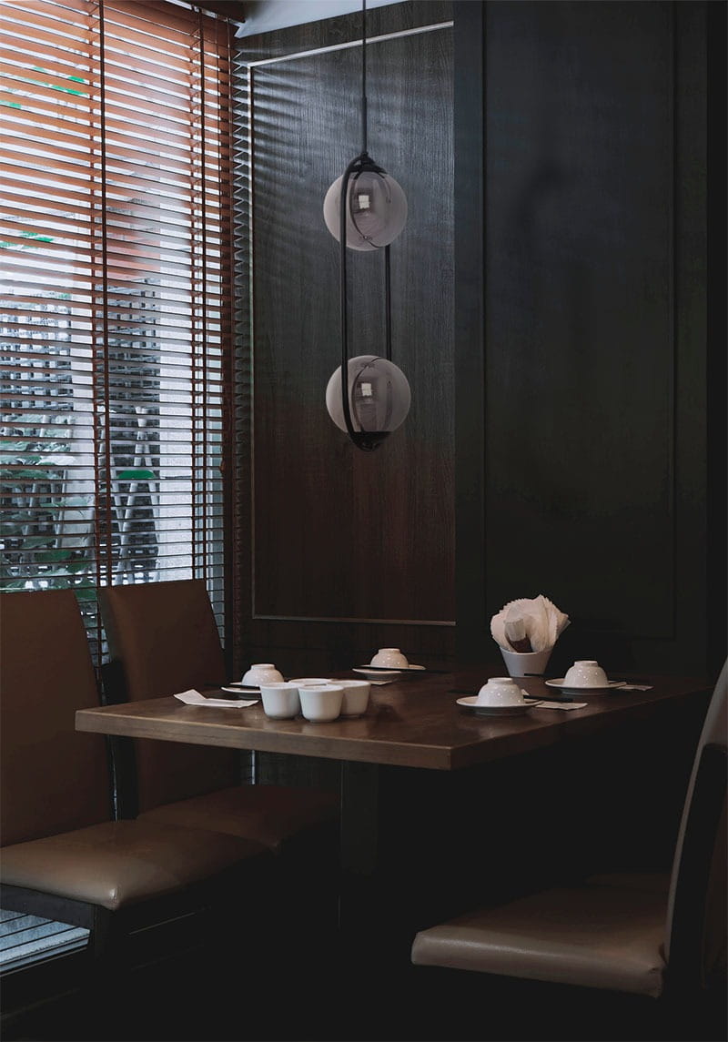 Lampa wisząca Davos 2xE14 w kolorze czarnym i grafitowym, z dwiema okrągłymi kloszami, zawieszona na czarnym przewodzie. Widoczna w kontekście eleganckiej jadalni z drewnianym stołem i brązowymi krzesłami.