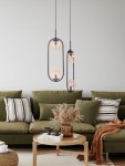 Lampa wisząca Venta z dwoma źródłami E14 w czarnej oprawie oraz bursztynowymi kloszami. Zawieszona w pokoju dziennym nad stolikiem, w otoczeniu zielonej kanapy, poduszek i dekoracyjnych akcesoriów.