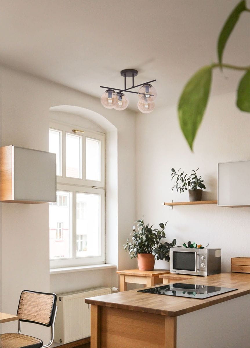 Czarna lampa sufitowa Delta z czterema oprawami E14, z bursztynowymi kloszami, zamontowana na suficie w kuchni. W tle drewniana kuchnia z roślinami doniczkowymi i oknem. Kąt ujęcia z dołu, eksponujący detal lampy.