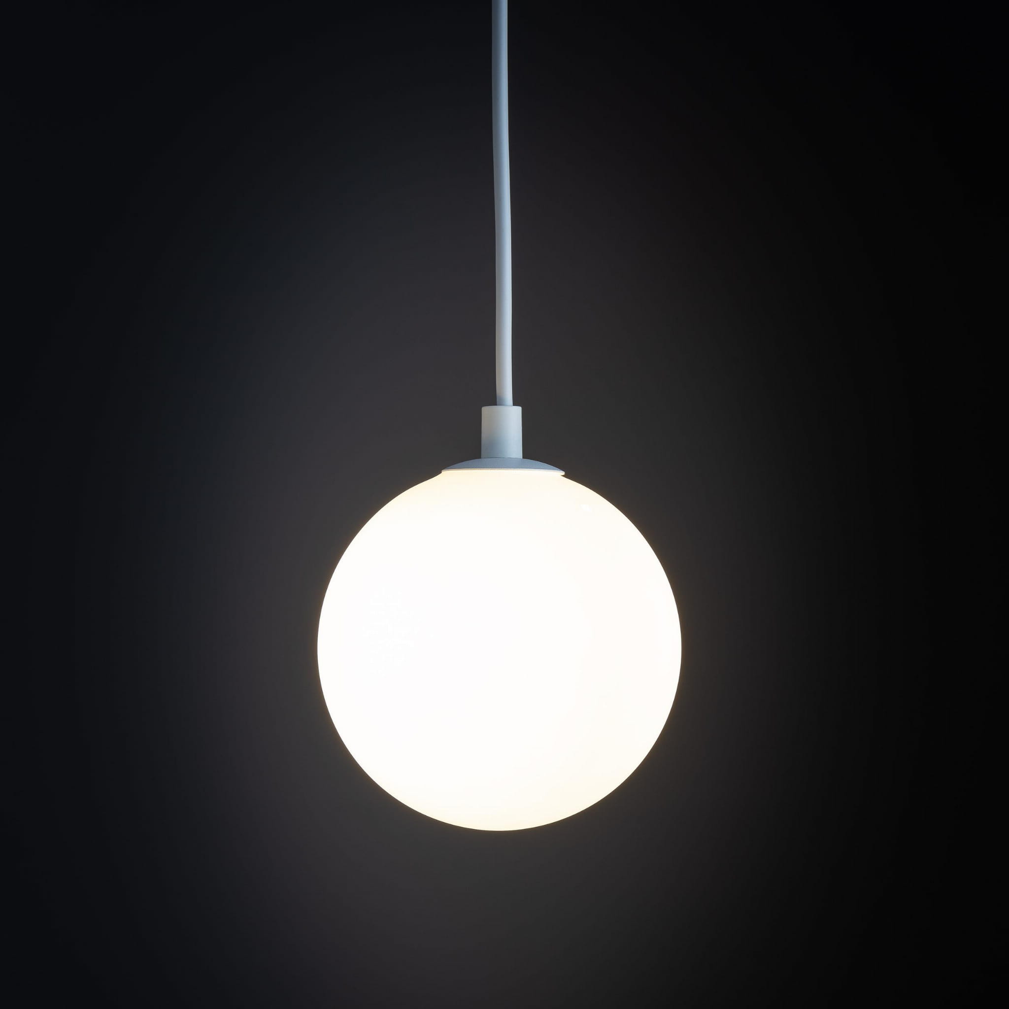 Lampa wisząca Tracer 1xG9 w kolorze białym, z okrągłym, matowym kloszem. Ujęcie z dołu, zawieszona na białym kablu. Tło ciemne, podkreślające prosty design. Idealna do nowoczesnych wnętrz.