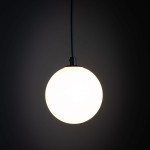 Lampa wisząca Tracer w kolorze czarnym i białym, z okrągłym, matowym kloszem, zawieszona na cienkim, czarnym przewodzie. Ujęcie zbliżone, pokazujące detal klosza na ciemnym tle. Przeznaczona do montażu na szynie, z miejscem na jedną żarówkę G9.