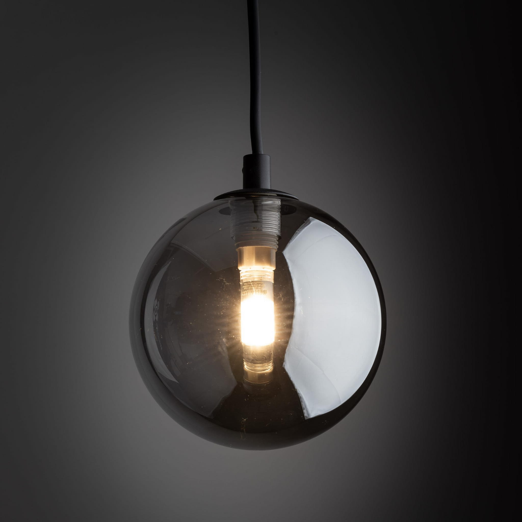 Lampa wisząca Tracer 1xG9 w czarnej/grafitowej obudowie z okrągłym, półprzezroczystym kloszem. Źródło światła widoczne wewnątrz. Produkt zawieszony na cienkim przewodzie, prezentowany na ciemnym tle.