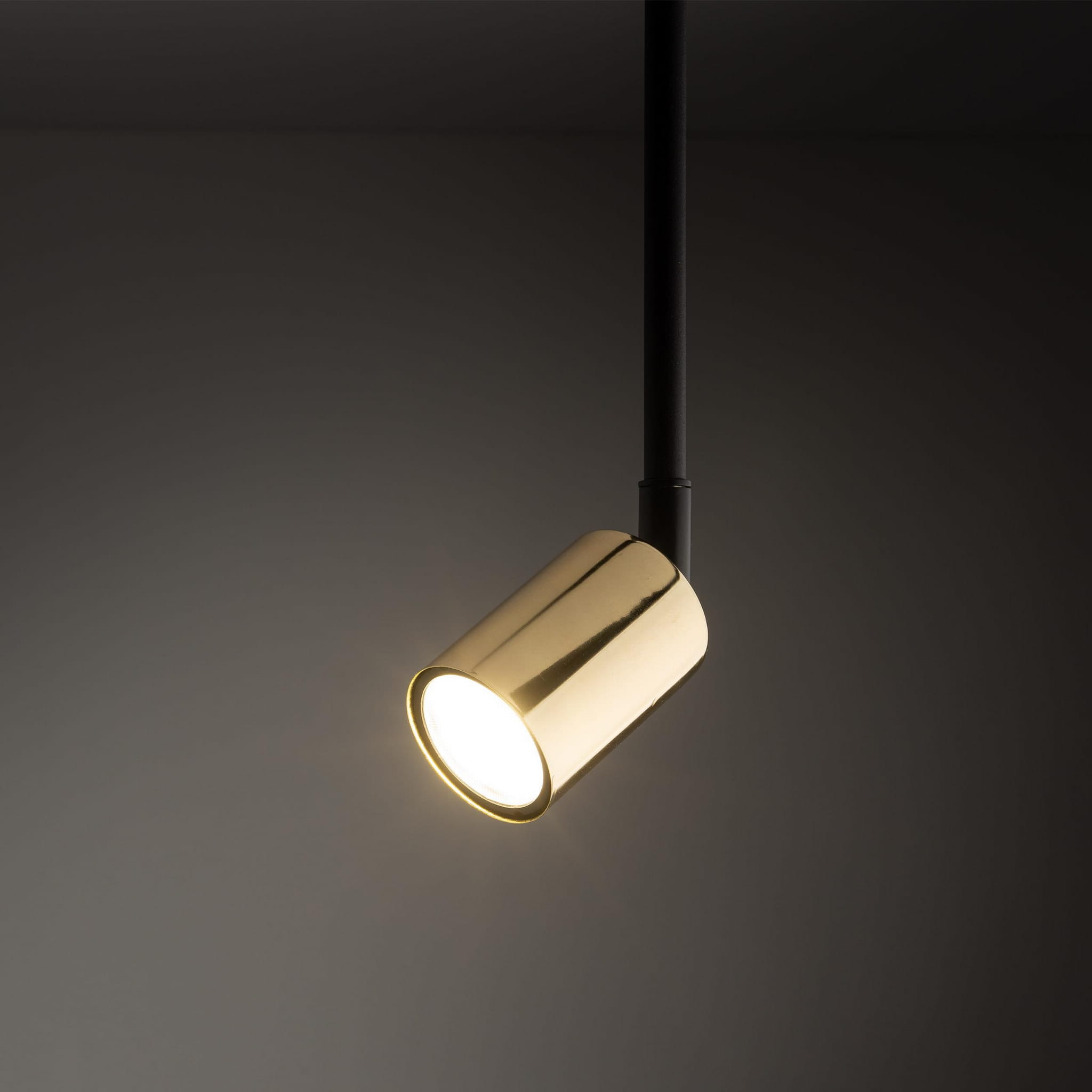 Reflektor Tracer w kolorze czarnym i złotym, zamontowany na szynie. W formie cylindrycznej, z błyszczącą złotą obudową i białym źródłem światła. Ujęcie z boku, ukazujące detale oraz stylowy design. Tło w ciemnym odcieniu.