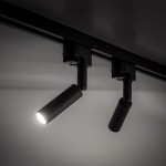 Reflektor Tracer 1xG9 w kolorze czarnym, montowany na szynie. Posiada cylindryczny kształt i regulowany kąt, emitując jasne światło. Widoczny element mocujący i dwa uchwyty. Tło neutralne, co podkreśla produkt.
