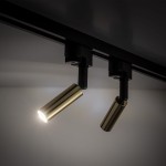 Reflektor Tracer 1xG9 w kolorze czarnym i złotym, zamontowany na szynie. Złota część lampy ma cylindryczny kształt, skierowana w dół, emitująca jasne światło. Tło jasne, minimalistyczne.