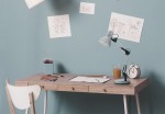 Lampka biurkowa Cosmo 1xE27 w kolorze chromu, z regulowanym ramieniem, stoi na drewnianym biurku. W tle błękitna ściana z rysunkami dzieci. Na biurku widoczne przybory do rysowania, szklanka z napojem i zegar.