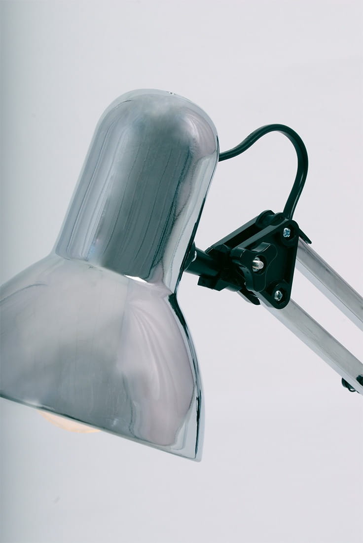 Lampka biurkowa Cosmo z metalowym kloszem w kolorze chromu, z ruchomym ramieniem i czarnymi akcentami. Ujęcie z boku, ukazujące detal klosza i mechanizm mocujący. Tło białe, co podkreśla nowoczesny design. Przeznaczona dla żarówki E27.