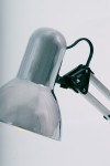 Lampka biurkowa Cosmo z metalowym kloszem w kolorze chromu, z ruchomym ramieniem i czarnymi akcentami. Ujęcie z boku, ukazujące detal klosza i mechanizm mocujący. Tło białe, co podkreśla nowoczesny design. Przeznaczona dla żarówki E27.