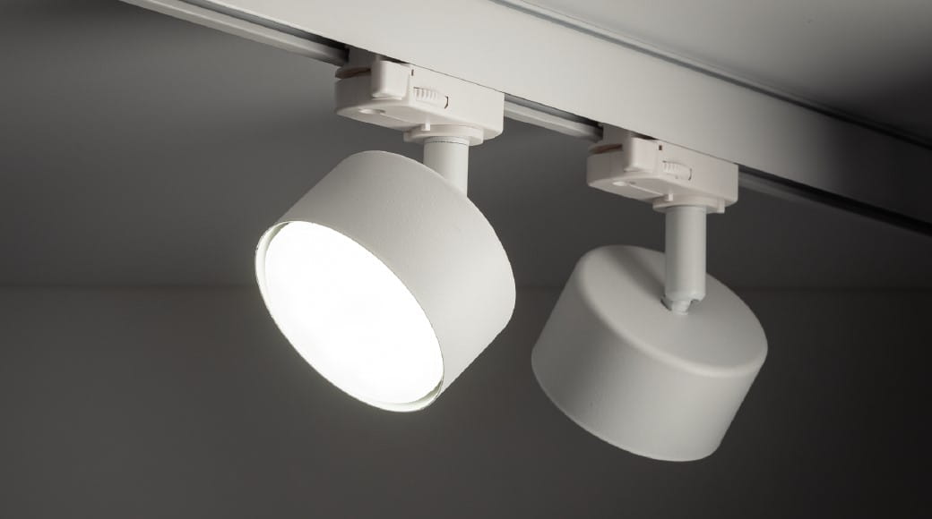 Reflektor Tracer 1xGX53 do szyny 3-fazowej w kolorze białym, zamontowany na szynie. Okrągła głowica z matowym wykończeniem, emitująca jasne światło. Widoczna jest także druga, nieaktywowana głowica. Tło ciemne, co podkreśla produkt.