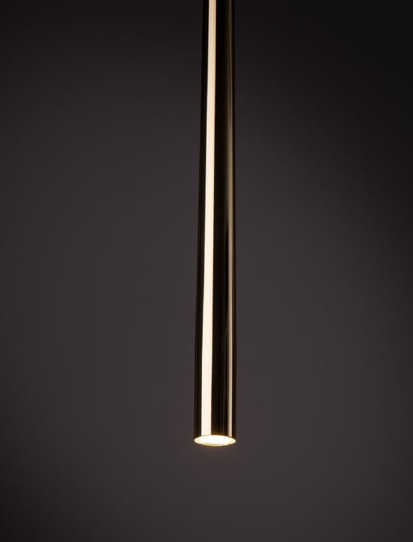 Lampa wisząca Tracer Piano w złotym kolorze, w kształcie smukłej, cylindrycznej tuby. Zawieszona pod kątem, z widocznym źródłem światła na dole. Minimalistyczny design, idealna do nowoczesnych wnętrz.