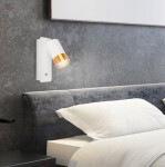 Klemens kinkiet z gniazdem USB, biały z złotym detalem. Zamontowany na ścianie, skierowany w dół, z jedną żarówką GU10. W tle widoczna szara ściana i łóżko z pościelą. Gniazdo USB umieszczone obok lampy.