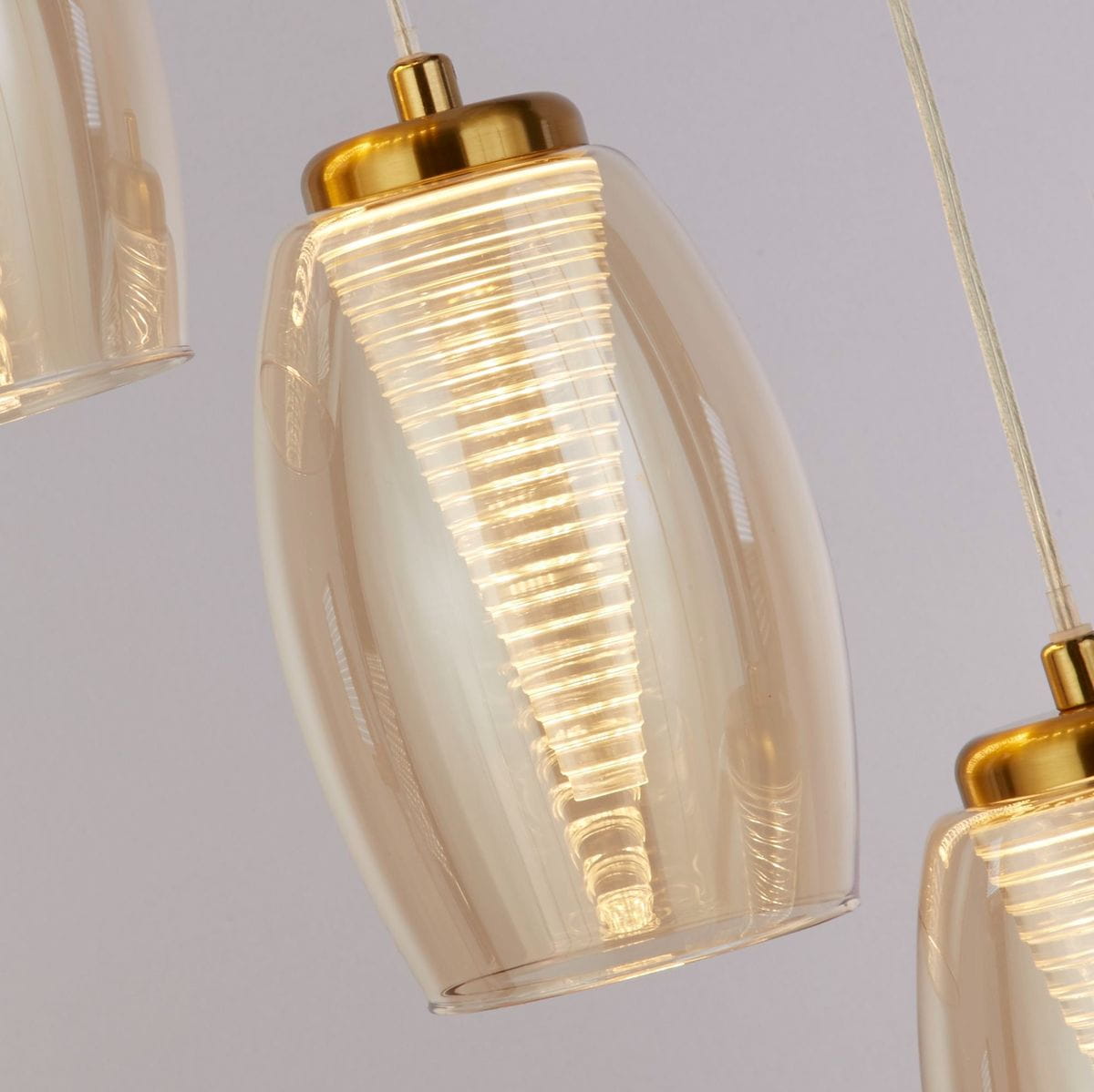 Lampa wisząca Cyclone z pięcioma źródłami LED, brązowa obudowa i bursztynowe klosze w kształcie elipsy. Złote detale przy górnej części, zawieszenie na przezroczystych linkach. Zbliżenie na detale klosza z widoczną strukturą.