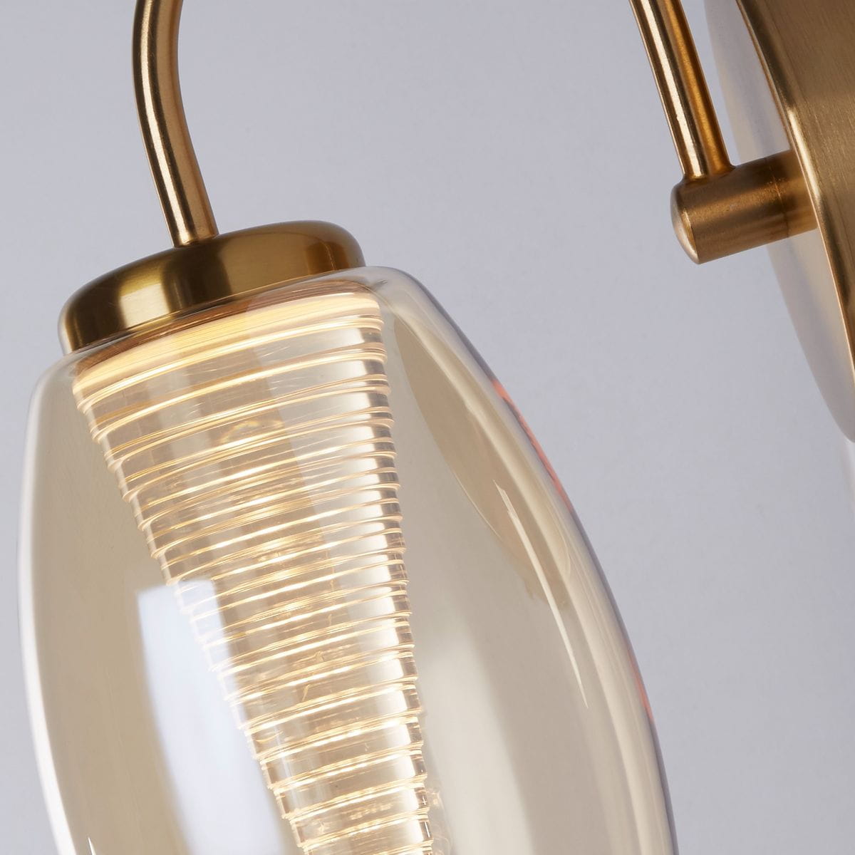 Kinkiet Cyclone 1xLED/6W w kolorze brązowym z bursztynowym kloszem, zbliżenie na szklany klosz o spiralnym wzorze. Metalowa baza w kolorze złotym, o eleganckim kształcie, montowany na ścianie. Tło w jasnym kolorze.