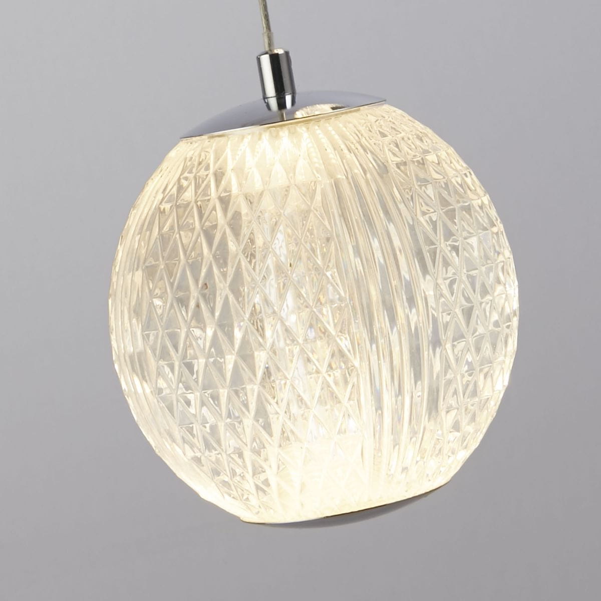 Lampa wisząca Allure z pięcioma źródłami LED, 28W, w chromowanej oprawie. Klosz w formie przezroczystej kuli z teksturą diamentową, zawieszony na cienkim przewodzie, emituje ciepłe światło. Tło w odcieniu szarości.