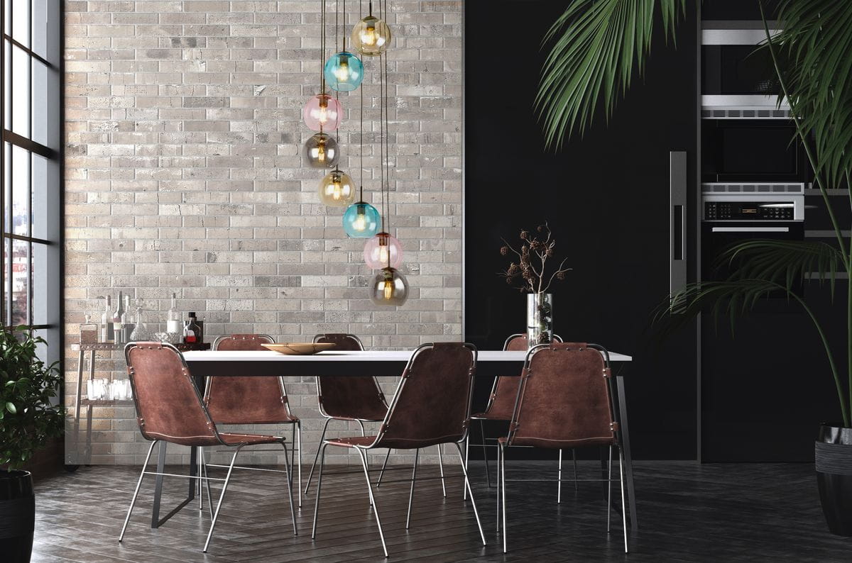 Lampa wisząca Mardi Gras II z 8 miejscami na żarówki E27, w kolorze czarnym. Zawieszona w nowoczesnym wnętrzu, obok stołu z brązowymi krzesłami. Szklane klosze w różnych kolorach (zielony, różowy, złoty) tworzą atrakcyjny efekt wizualny.