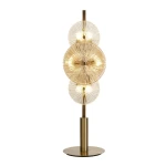 Lampa stołowa Wagon Wheel w brązowej i bursztynowej kolorystyce z sześcioma żarówkami G9. Okrągłe klosze z przeźroczystego szkła z teksturowanym wzorem, na metalowej podstawie w kolorze złotym, ustawiona w pionie.