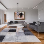 Lampa wisząca Lugano w kolorze chromu, z jednym źródłem światła E14, zawieszona na cienkim kablu. Produkt umieszczony w nowoczesnym wnętrzu z szarymi sofami i okrągłym stolikiem na tle abstrakcyjnego obrazu.