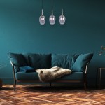 Lugano lampa wisząca 3xE14 w kolorze chromu, składająca się z trzech przezroczystych kloszy o kształcie kropli, zawieszona na cienkich przewodach. Lampa umieszczona nad ciemnoniebieską sofą w stylowym wnętrzu z drewnianą podłogą.
