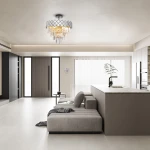 Lampa sufitowa Carisma 9xE14 w chromowanym wykończeniu, z dekoracyjnymi, przezroczystymi kryształkami, wisząca w nowoczesnym wnętrzu. Ujęcie z dołu, w tle widoczna kuchnia oraz wygodna sofa.