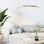 Lampa wisząca Breno D60 o złotym kolorze, z okrągłym metalowym ramieniem i wbudowanym źródłem światła LED 28W. Zawieszona nad sofą w jasnym wnętrzu, otoczona roślinnością i nowoczesnym stolikiem.