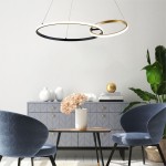 Lampa wisząca Rando z dwoma okręgami, czarna i złota, zawieszona nad stolikiem. W tle szara komoda z dekoracjami, białe wazony i roślina. Oświetlenie LED, nowoczesny design.