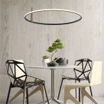 Lampa wisząca Claud w kolorze czarnym, z okrągłym, cienkim ramieniem LED o mocy 42W. Zawieszona nad okrągłym stołem, w otoczeniu nowoczesnych krzeseł. Tło w jasnym odcieniu drewna, z roślinnością w doniczkach.