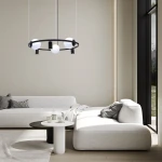 Lampa wisząca Orbit z trzema oprawami E27 i trzema GU10 w kolorze czarnym i białym. Okrągła konstrukcja z mlecznymi kuleczkami, zawieszona na cienkich linkach. Produkt umieszczony w nowoczesnym wnętrzu z jasną sofą i okrągłym stołem.