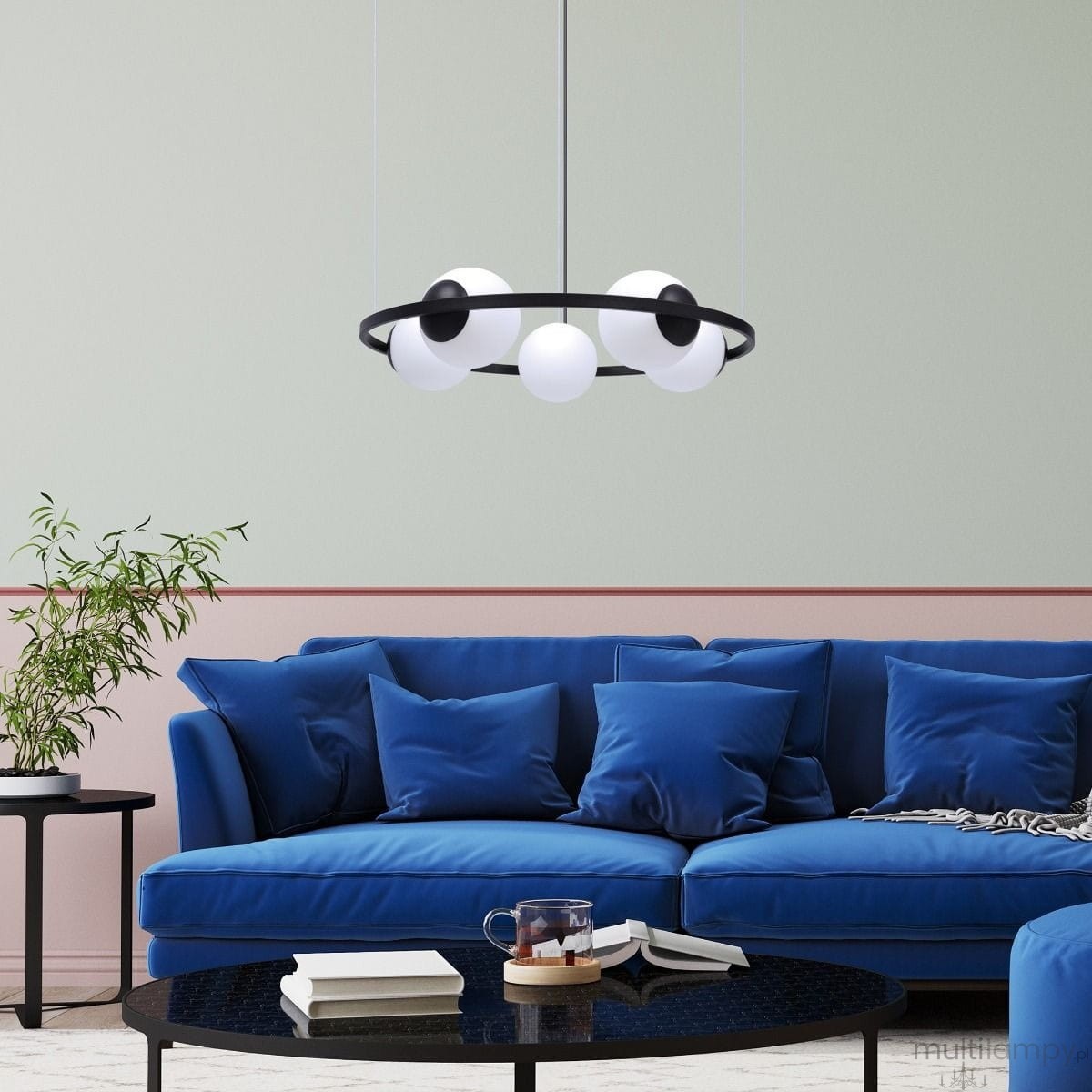Lampa wisząca Orbit w kolorze czarnym i białym, z pięcioma oprawami E27, zawieszona na cienkich linkach. Kształt okrągły, z białymi kulistymi kloszami i czarnym pierścieniem. W tle niebieska sofa i stół kawowy.