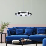 Lampa wisząca Orbit w kolorze czarnym i białym, z pięcioma oprawami E27, zawieszona na cienkich linkach. Kształt okrągły, z białymi kulistymi kloszami i czarnym pierścieniem. W tle niebieska sofa i stół kawowy.