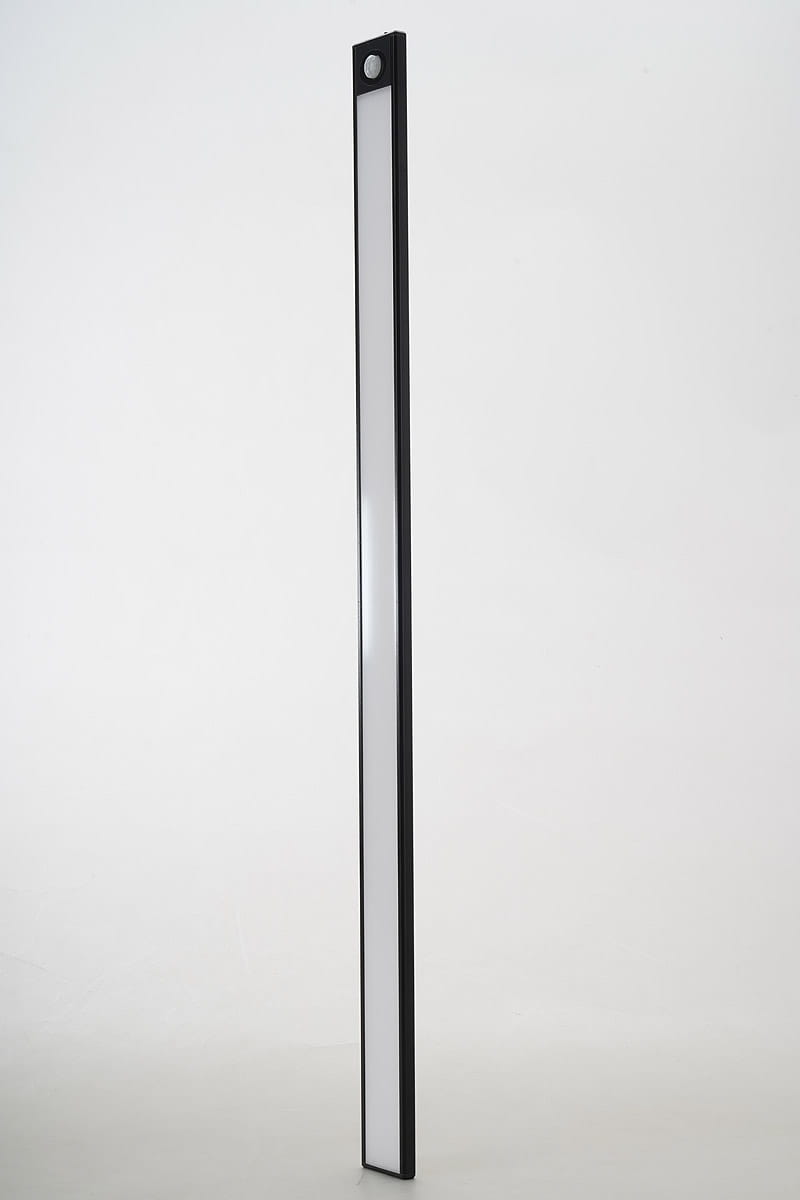 Listwa podszafkowa LED 80 cm w kolorze czarnym z czujnikiem ruchu. Produkt ma prostokątny kształt, z białą, przezroczystą częścią emitującą światło. Ujęcie z boku, ukazujące smukłą formę i czujnik na górze. Tło jasne, minimalistyczne.