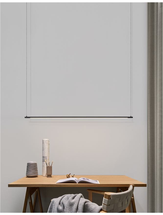 Lampa wisząca Buga w kolorze czarnym, z jedną diodą LED o mocy 20W. Produkt zawieszony w poziomie, z minimalistycznym designem, nad drewnianym biurkiem w jasnym otoczeniu. Kabel w kolorze czarnym, prosta forma bez dodatkowych zdobień.