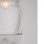 Lampa wisząca Ahigal z przezroczystym kloszem w pionowe żłobienia, z mocowaniem na żarówkę E14. Klosz w kształcie lekko zwężającym się ku dołowi, z dekoracyjną krawędzią u dołu. Tło białe, produkt widoczny z boku.