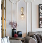 Kinkiet Ahigal 1xE14 w kolorze złotym, z okrągłym kloszem w szklanym, teksturowanym wykończeniu. Zawieszony na ścianie, w aranżacji z dekoracyjnymi wazonami i kompozycją roślinną, na tle eleganckiej ściany z detalami architektonicznymi.