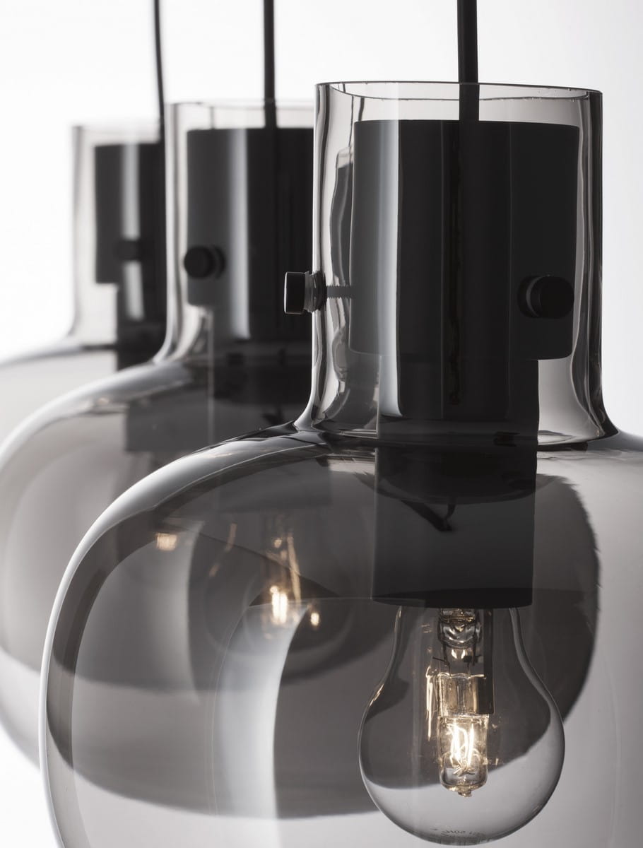 Lampa wisząca Padre w kolorze czarnym z trzema żarówkami E27. Szklane klosze w ciemnym odcieniu, z widocznymi żarówkami. Produkt zawieszony na cienkim kablu, z metalowym mocowaniem. Detale w minimalistycznym stylu.